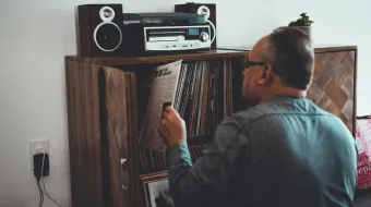Man in Gray Longsleeve Shirt Holding Music Album in Front of Brown Wooden Book Case