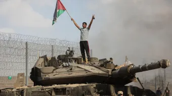 Palestinian on top of a tank holding Palestine flag